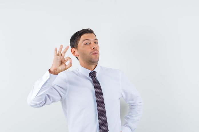young male showing ok gesture in white shirt,tie and looking pleased , front view. roja dalam Islam
